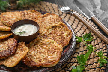 Plate of tasty zucchini fritters with sour cream on table