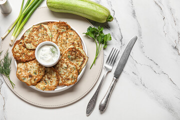 Plate of tasty zucchini fritters with sour cream on white marble background