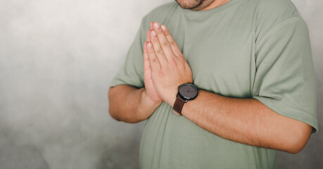 Close up of young man in green t-shirt greeting by doing namaste with folded hands in greeting pose. Hand symbol means to pay respect and greeting others.