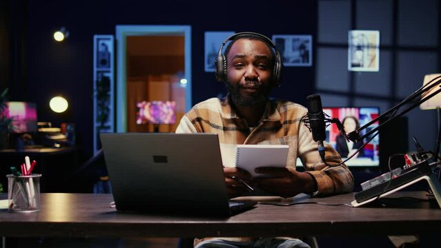 African american media star using outlined ideas on notebook to film vlog channel intro for online streaming platforms. Man following discourse script on paper, presenting today video topic