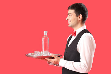 Male waiter with glasses and bottle of vodka on red background