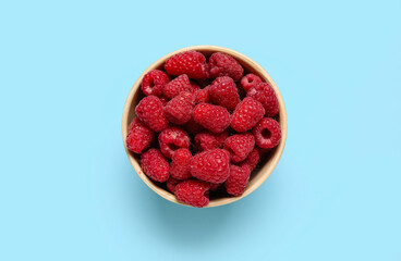 Bowl with fresh raspberries on blue background