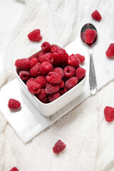 Bowl with fresh raspberry and spoon on light background, closeup