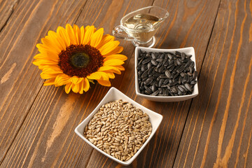 Sunflower, bowls with seeds and oil on wooden background