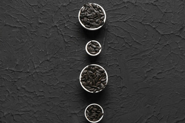 Fototapeta na wymiar Bowls with sunflower seeds on black background