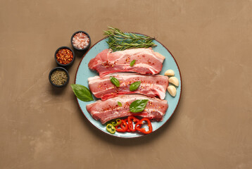 Plate with raw pork ribs, herbs and spices on color background