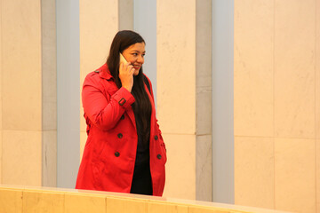 40-year-old Latina woman in a red trench coat uses her cell phone to work, make calls, send messages, make payments and shop online