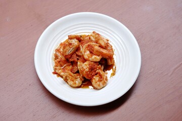Schezwan Prawns in white plate with wooden background. Schezwan Prawns is indo-chinese cuisine curry dish with prawns or shrimps roasted in Schezwan Sauce. Udang saos Padang 