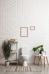 Interior of light restroom with ceramic toilet bowl, shelving unit and houseplants near white brick wall