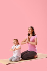 Obraz na płótnie Canvas Beautiful mother and her cute little girl with mats doing yoga on pink background