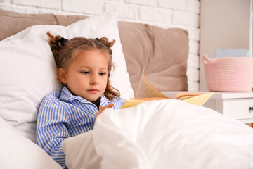 Cute little girl reading book in bedroom