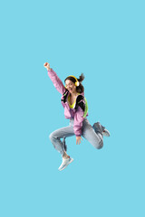 Stylish young woman in headphones jumping on blue background
