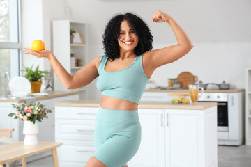 Sporty adult woman with orange flexing in kitchen