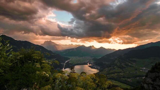 Orange sun rays fall on Alpine Lake Walensee at golden hour reflecting vibrant sky