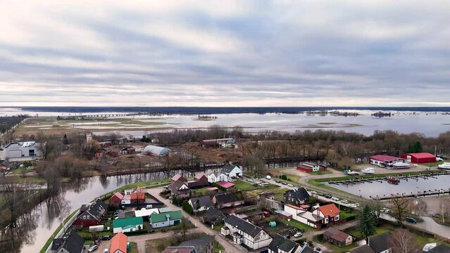 Aftermath of winter flooding in town outskirts of Silute Lithuania, calm water reflects sky and leafless trees