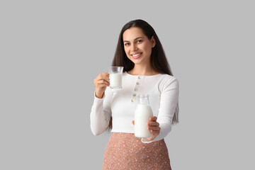 Young woman with glass and bottle of tasty milk on grey background