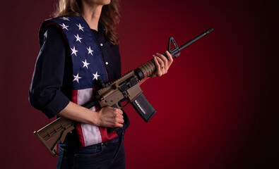 Armed citizen holding an AR rifle with an American flag over her shoulder