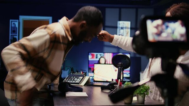 African American Influencer And Woman Arriving In Home Studio, Starting Podcasting Session, Greeting Each Other. Joyful Presenter Fist Bumping Guest, Ready To Begin Recording For Live Online Show