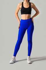 Sporty young woman in blue leggings on light background