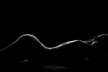 Silhouette of attractive young woman in underwear lying on dark background - Powered by Adobe
