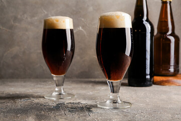 Glasses and bottles of cold dark beer on table against grey grunge background