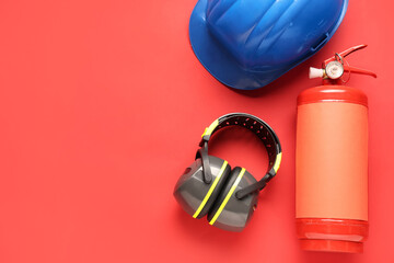 Fire extinguisher, hearing protectors and helmet on red background