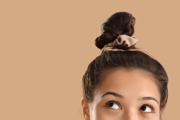 Young Asian woman with bun and scrunchy on beige background, closeup