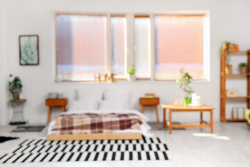 Blurred view of light bedroom with bed, tables and window
