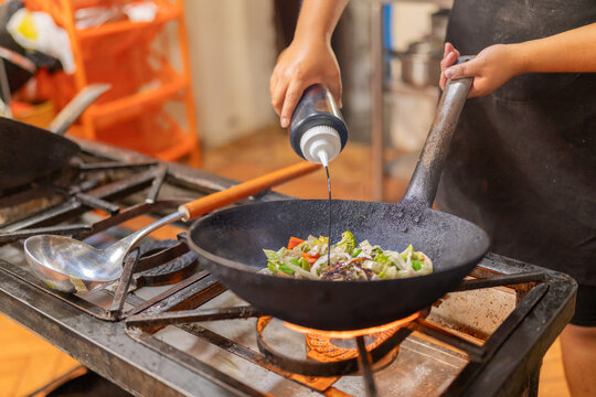 Chef adding soy sauce to vegetables in a pan