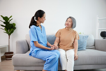 caregiver or nursing home holding hands and talking with senior woman on sofa