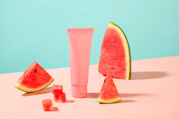 Minimal scene of watermelon cut in slices surrounded a cosmetic tube in pink color. Branding mockup. Watermelon (Citrullus lanatus) is enriched with the goodness of vitamin A, B, and E