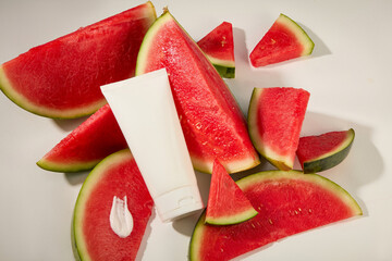 View from above of a cosmetic tube lying on some large watermelon slices. A smear of cream featured...