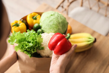 Young woman with paper bag of fresh vegetables in kitchen, closeup