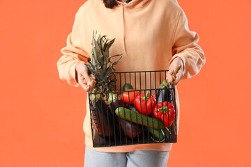 Young woman with basket of healthy food on orange background, closeup