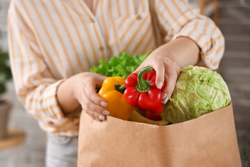 Young woman with paper bag of fresh vegetables in kitchen, closeup