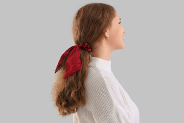 Young redhead woman with ponytail and scrunchy on light background