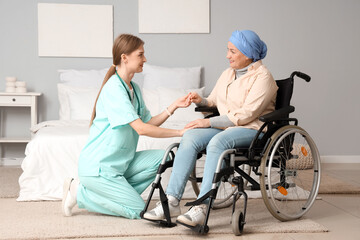 Mature woman after chemotherapy in wheelchair with nurse holding hands at home. Stomach cancer concept