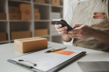 Fototapeta premium Smartphones are being used to do various activities to promote sales to stores, owner of an online store packs products into parcel boxes based on orders from online sales sites.
