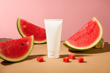 Front view of a white plastic tube container cream or facial cleanser displayed with fresh watermelon slices on a pink background. Mockup bottle for design, advertising product