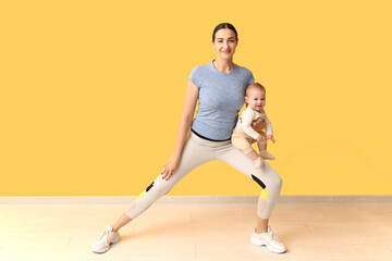 Beautiful young sporty woman with her little baby practicing yoga near yellow wall