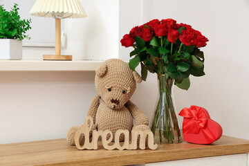 Beautiful bouquet of roses with gift box and home decor on commode near white wall. Valentine's Day...
