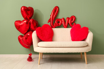 Stylish sofa with heart-shaped balloons and pillows near green wall. Valentine's Day celebration