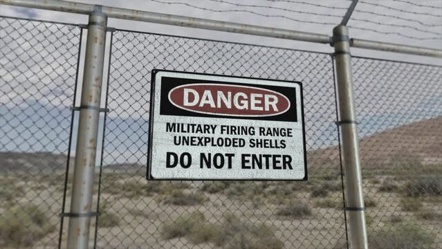 High quality 3D CGI render with a smooth dollying-out shot of a chainlink fence at a high security installation in a desert scene, with a Danger Military Firing Range sign