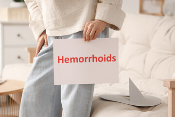 Mature woman with word HEMORRHOIDS and paper thumbtack on sofa at home, closeup
