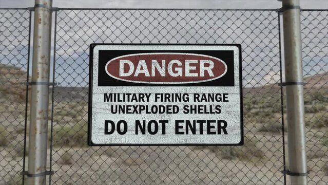 High quality 3D CGI render with a smooth dollying-in shot of a chainlink fence at a high security installation in a desert scene, with a Danger Military Firing Range sign