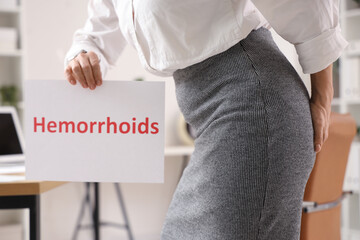 Mature businesswoman with word HEMORRHOIDS in office, closeup