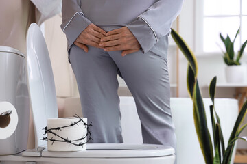 Mature woman and paper with barbed wire on toilet bowl in restroom, back view. Hemorrhoids concept