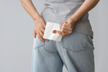 Mature woman holding paper with blood spot on light background, back view. Hemorrhoids concept
