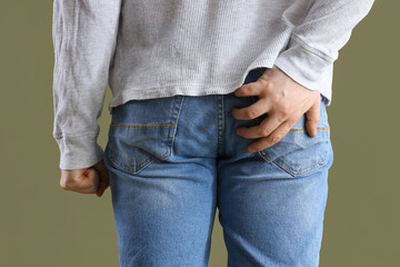 Young man with hemorrhoids on green background, back view