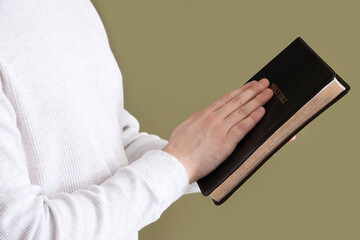 Young man with Holy Bible praying on green background, closeup